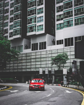 A vibrant red sedan cruising through a bustling city street at sunset