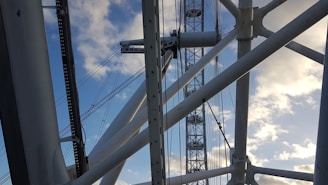 Large metal structures and cables intersect against a backdrop of a clear blue sky with scattered clouds, suggesting an architectural or engineering structure.