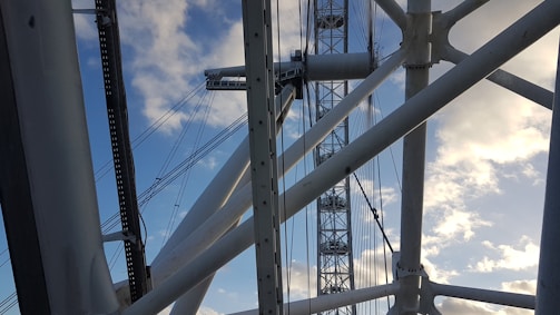 Large metal structures and cables intersect against a backdrop of a clear blue sky with scattered clouds, suggesting an architectural or engineering structure.