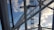 Large metal structures and cables intersect against a backdrop of a clear blue sky with scattered clouds, suggesting an architectural or engineering structure.