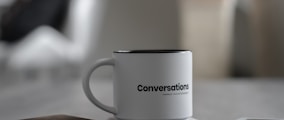 white conversations printed mug near smartphone