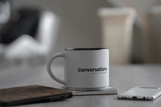 white conversations printed mug near smartphone