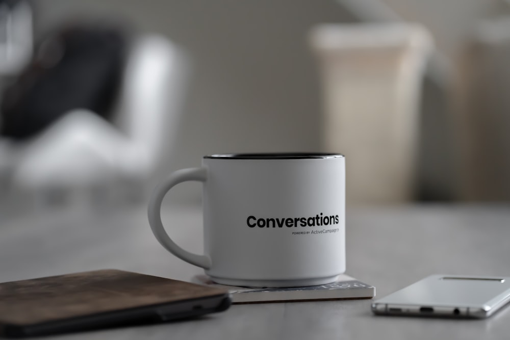 white conversations printed mug near smartphone