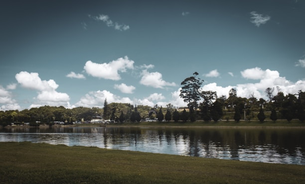 A serene landscape with a calm lake reflecting the sky and surrounding trees.