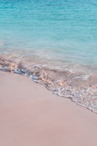 Calm turquoise waves gently washing over smooth beige sand.