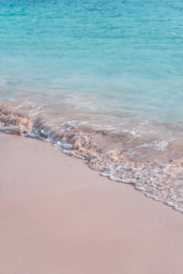 A peaceful turquoise wave gently washing over white sandy shore under a soft morning light.