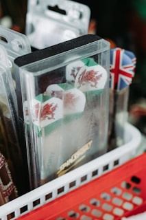 A close-up of dart flights in packaging featuring Welsh dragons and a Union Jack motif, placed in a red and white basket with other dart accessories.