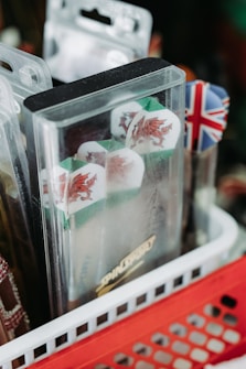 A close-up of dart flights in packaging featuring Welsh dragons and a Union Jack motif, placed in a red and white basket with other dart accessories.