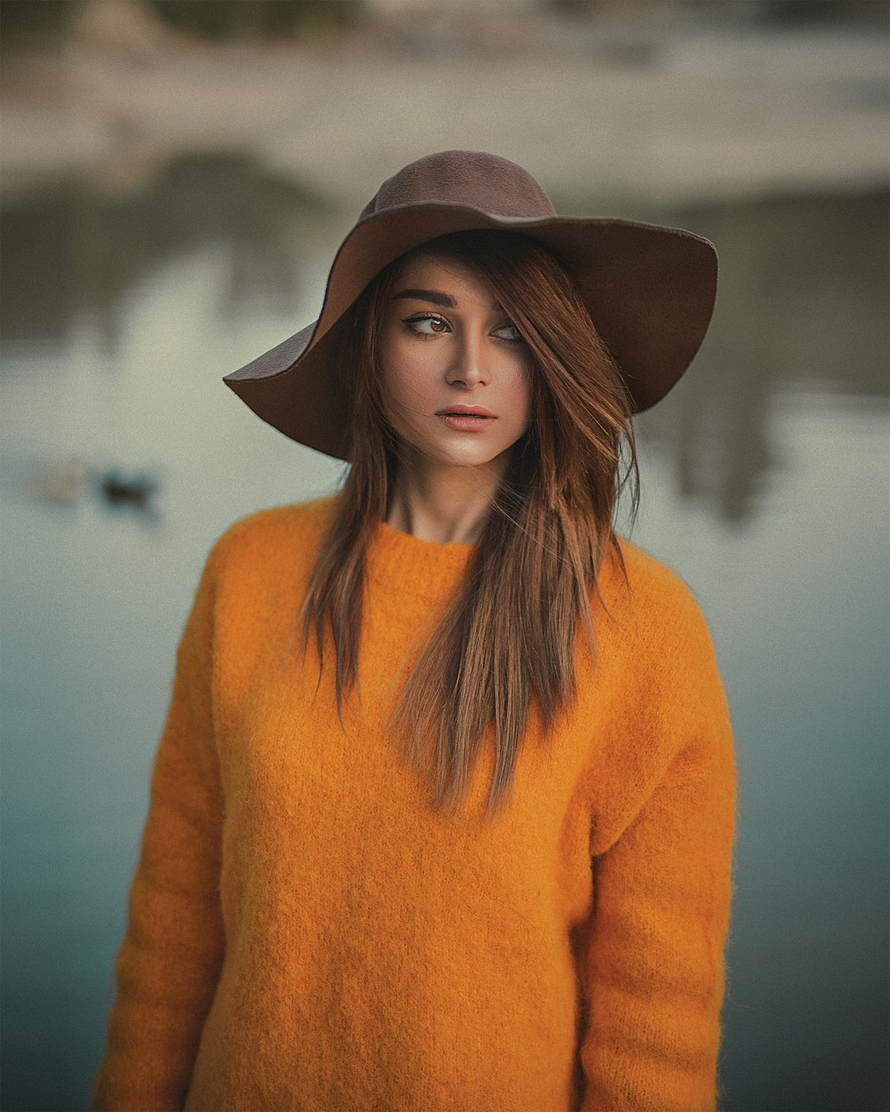 woman wearing orange sweater and brown hat standing and facing her right side