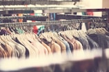 A clothing rack is filled with various garments hanging on hangers, showcasing a range of colors and textures. The clothes appear to be neatly organized, and there is an abundance of knitted and sweater-like items.