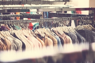 A clothing rack is filled with various garments hanging on hangers, showcasing a range of colors and textures. The clothes appear to be neatly organized, and there is an abundance of knitted and sweater-like items.