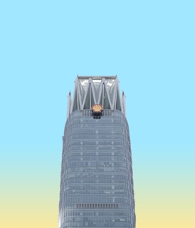 A skyscraper with a distinctive modern design features a prominent Shell logo near the top. The building is set against a bright sky that transitions from blue to a pale yellow near the horizon.