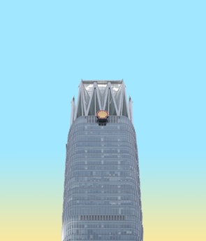 A skyscraper with a distinctive modern design features a prominent Shell logo near the top. The building is set against a bright sky that transitions from blue to a pale yellow near the horizon.