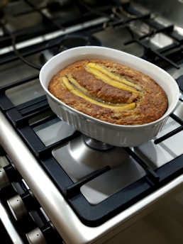 Freshly baked banana cake with a golden crust on a white ceramic dish, surrounded by ripe bananas