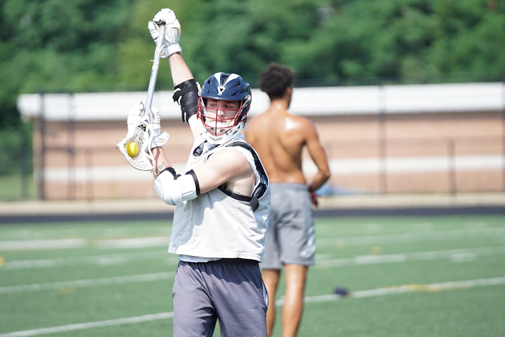 person holding lacrosse stick across topless man wearing gray shorts