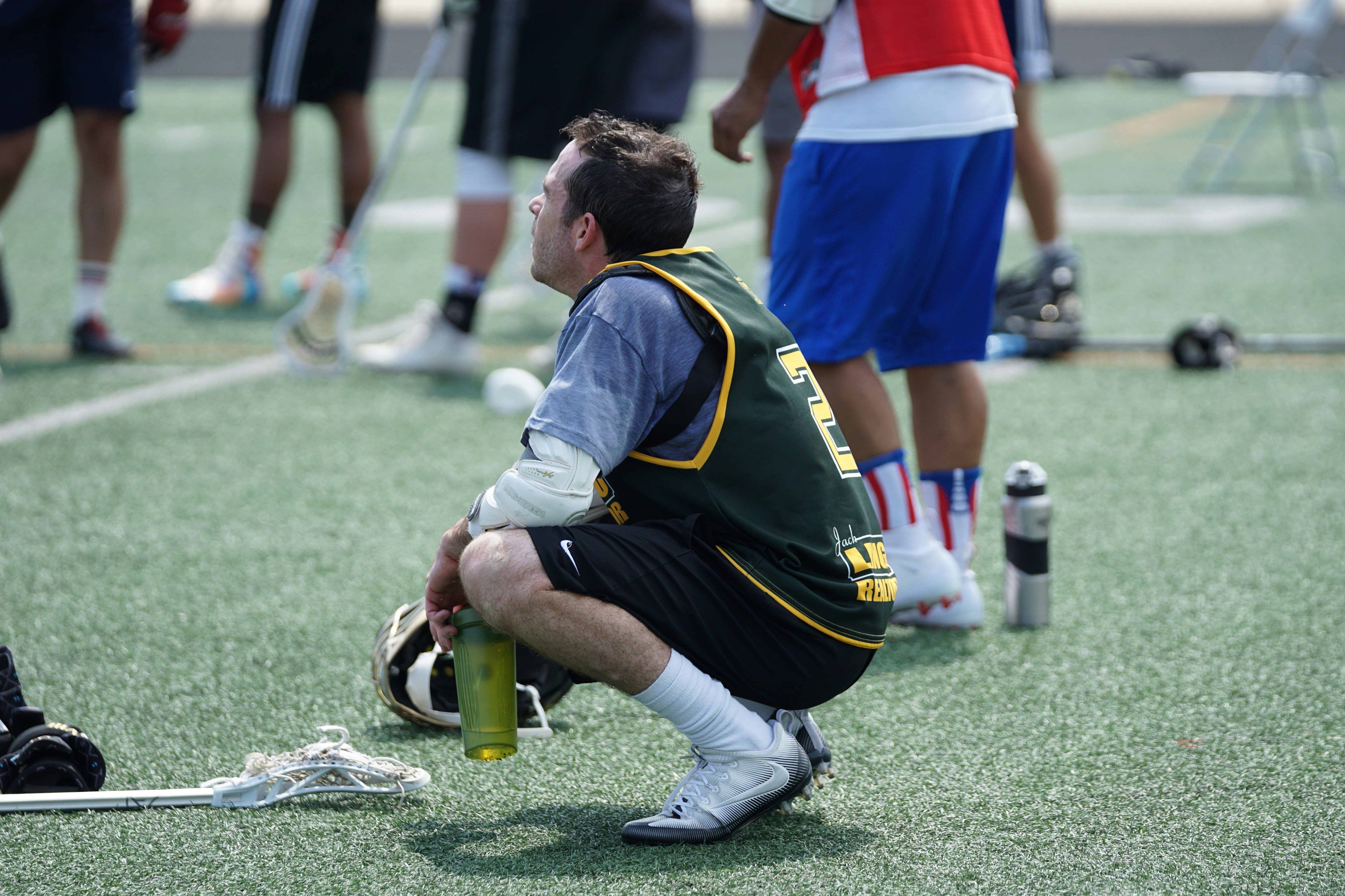 man squat while holding water tumbler after playing lacrosse