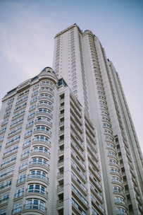 A modern high-rise building with a series of windows lined up in an orderly fashion. The design features curved elements and intricate patterns, exemplifying contemporary architecture against a clear blue sky.