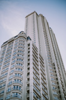 A modern high-rise building with a series of windows lined up in an orderly fashion. The design features curved elements and intricate patterns, exemplifying contemporary architecture against a clear blue sky.