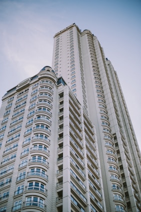A modern high-rise building with a series of windows lined up in an orderly fashion. The design features curved elements and intricate patterns, exemplifying contemporary architecture against a clear blue sky.