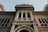A detailed view of an architectural facade featuring intricate patterns and decorative arches, with an emphasis on historical and elaborate designs typical of classical architecture. The structure includes ornate windows and a mix of geometric and floral motifs on its surface.