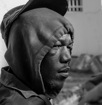 Black and white photo of a model wearing an oversized hoodie and cap, standing against a stark urban backdrop.