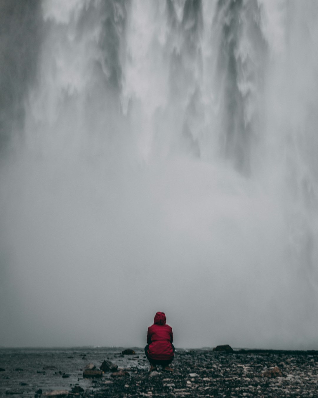 person in red jacket facing waterfalls