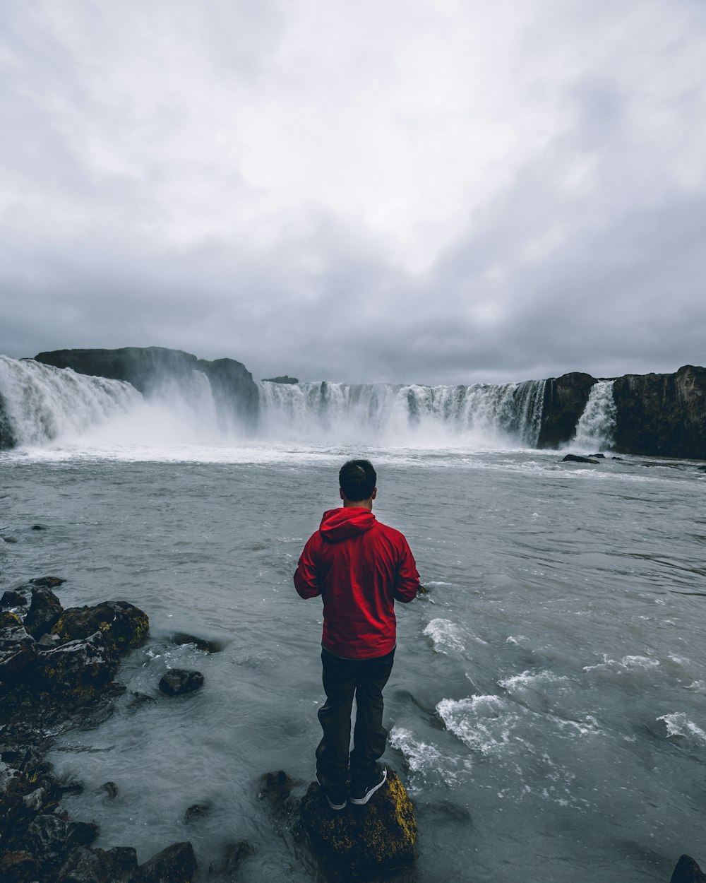 person standing in a rock near waterfalls during daytime