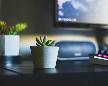 A sleek, compact desktop air purifier glowing softly on a modern office desk beside a laptop and a small potted plant.