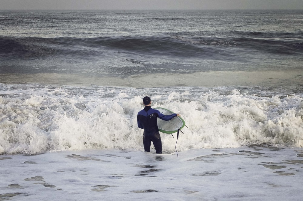 man wearing wetsuit carrying surfboard