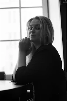 A contemplative black and white portrait of a writer seated by a window, bathed in soft natural light.