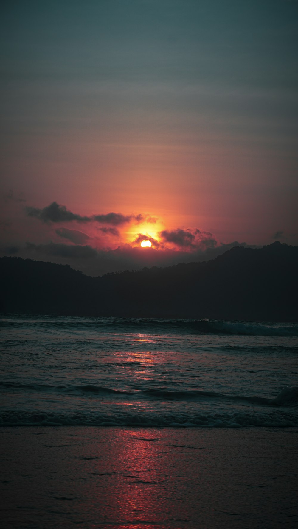 o sol está se pondo sobre o oceano em um dia nublado