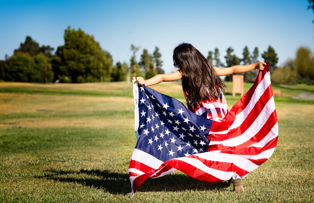 niña sosteniendo la bandera de EE.UU. en la pradera