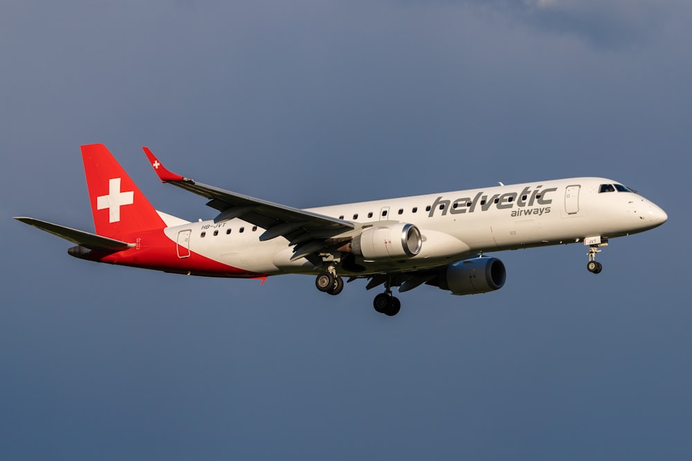 Avion blanc et rouge volant sous un ciel nuageux