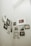 A collection of framed photographs and artworks is arranged on a light-colored wall. The display includes various sizes and styles of frames, featuring family photos, portraits, and decorative letters 'K' and 'R'. The images include a flower, a forest scene, and people in different poses.