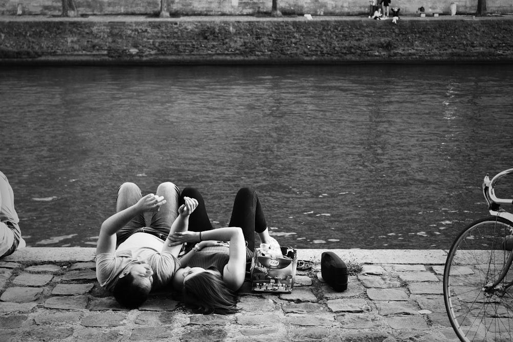 man and woman lying on ground near body of water