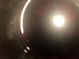 A bright, circular light source is centered within a dark, round, reflective background. Red and dark shades subtly blend around the circle, with brighter reflections on the edges, giving a tunnel-like effect.