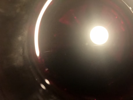 A bright, circular light source is centered within a dark, round, reflective background. Red and dark shades subtly blend around the circle, with brighter reflections on the edges, giving a tunnel-like effect.