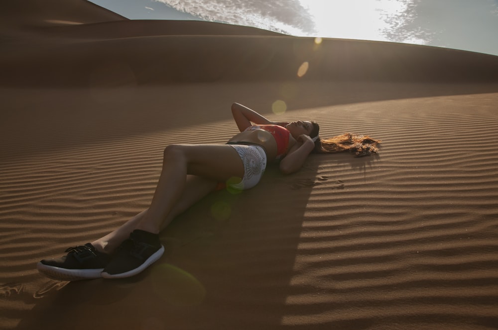 woman in red crop top and white denim short shorts lying on brown sand