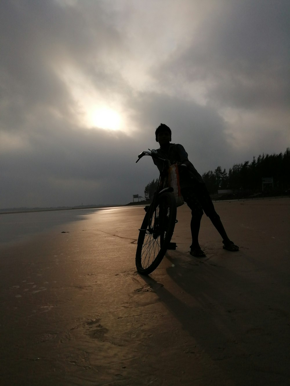 silhouette of person standing beside mountain bike near brown sand during daytime