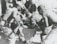 A group of individuals are engaged in moving or assisting a person on a stretcher. The scene appears to involve military personnel, possibly during a rescue or emergency situation. The environment suggests they might be near a vehicle or aircraft.