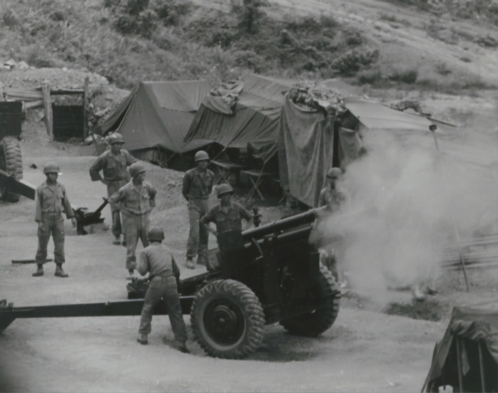 grayscale photo of men standing near cannon