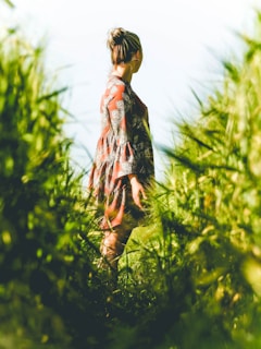 A model posing outdoors wearing a flowing dress with subtle patterns, surrounded by greenery.