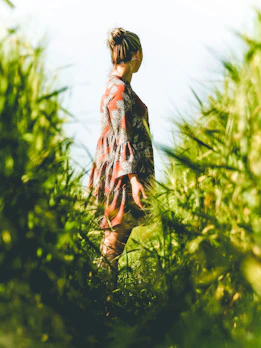 A model wearing a flowing organic cotton dress, standing amidst tall grasses.
