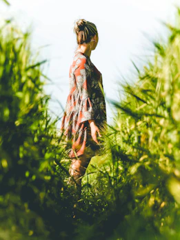 A model wearing a flowing organic cotton dress, standing amidst tall grasses.
