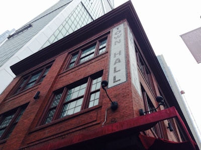 A tall, historic red brick building with multiple windows and a sign that reads 'Town Hall' in white bricks. Surrounding the structure are modern skyscrapers with reflective glass facades. The scene captures an interesting contrast between old and new architecture.