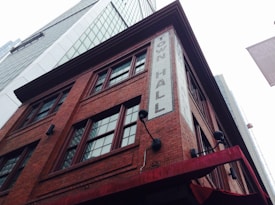 A tall, historic red brick building with multiple windows and a sign that reads 'Town Hall' in white bricks. Surrounding the structure are modern skyscrapers with reflective glass facades. The scene captures an interesting contrast between old and new architecture.
