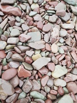 A collection of smooth, rounded stones in various shades of red, green, and gray. These stones vary in size and are packed closely together, showcasing a natural and earthy texture.