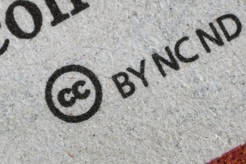 Close-up view of a Creative Commons license symbol with the letters 'cc' inside a circle, followed by 'BY NC ND' printed on what seems to be a textured paper background.