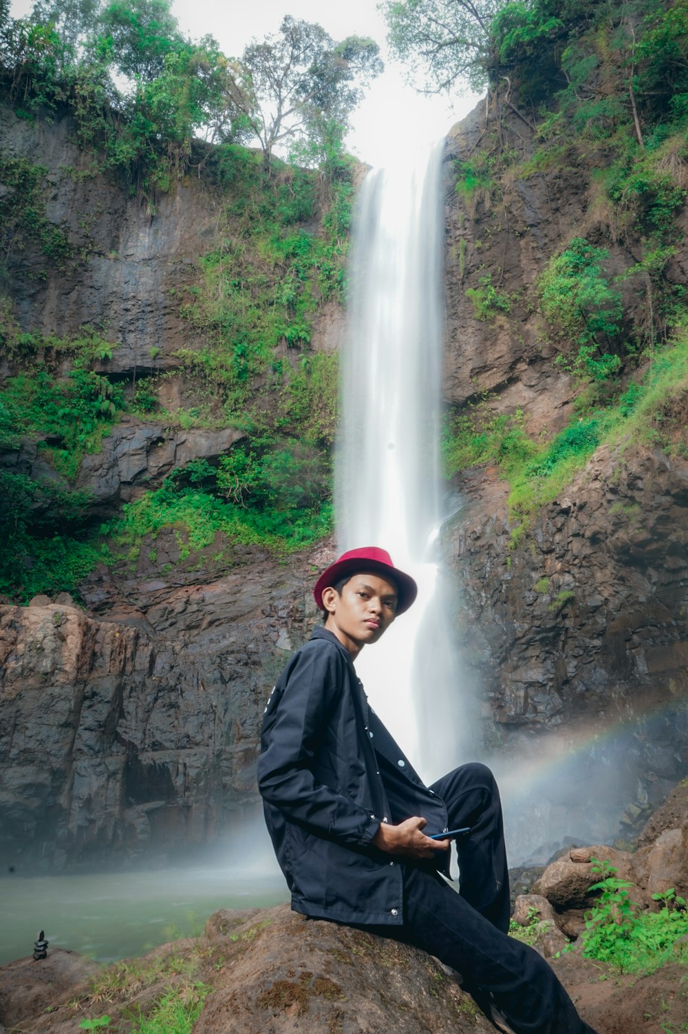 men sitting in a rock near water fall during daytime