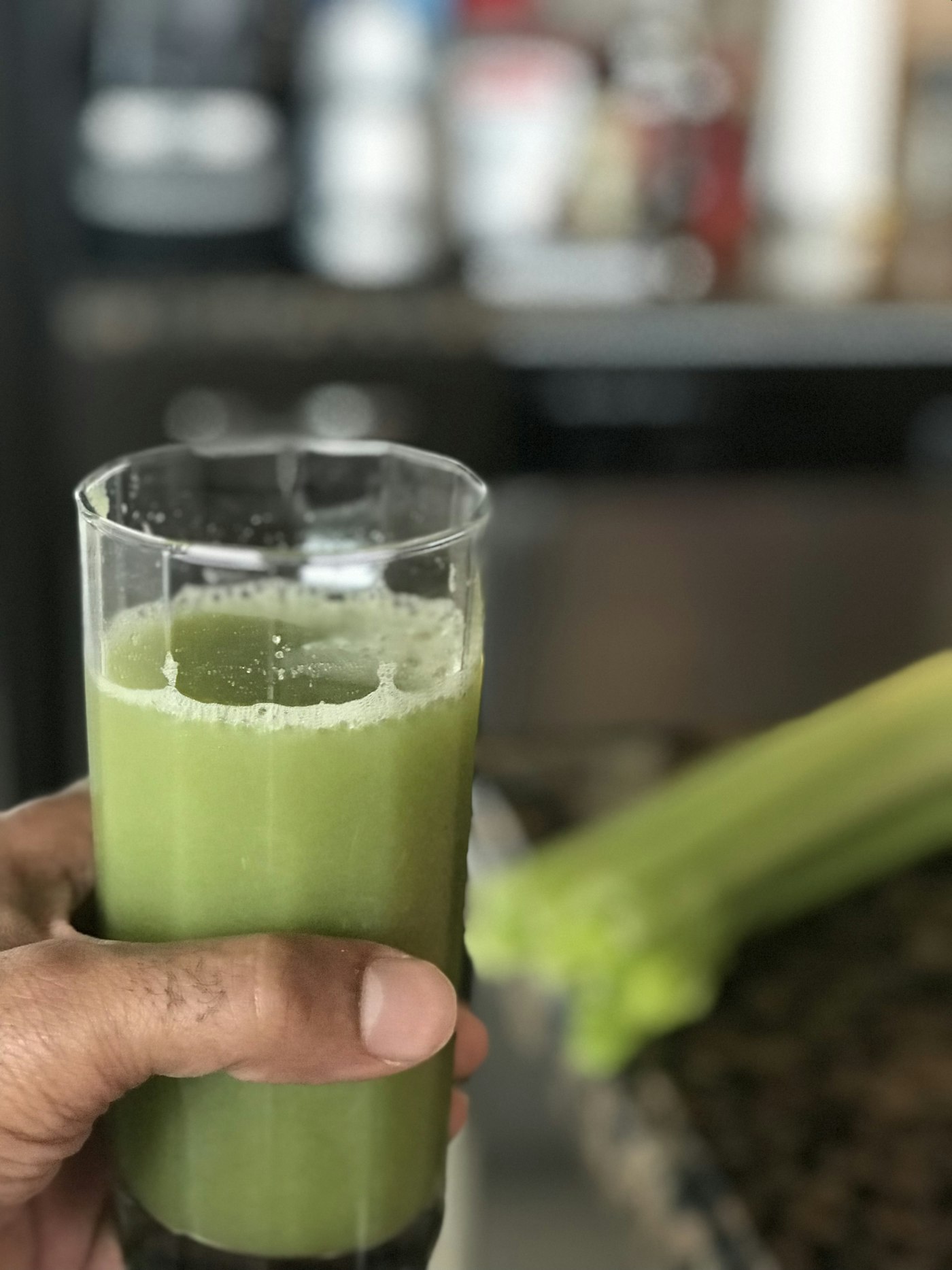 A glass of green celery juice with a fresh celery stalk